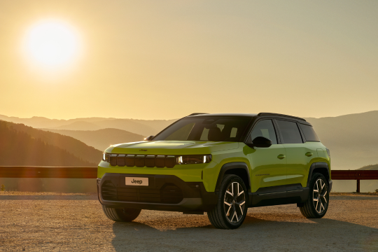 gelbes Auto steht auf Panoramastraße mit Blick über Berglandschaft und Sonnenuntergang
