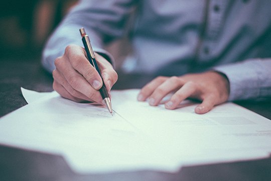 Mann sitzt am Tisch und unterzeichnet einen Vertrag