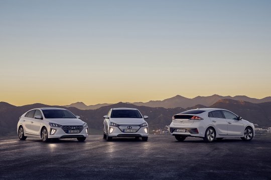 Hyundai IONIQ Elektro IONIQ Plug-In Hybrid und IONIQ Hybrid stehen auf einem Parkplatz vor Bergen bei Sonnenuntergang